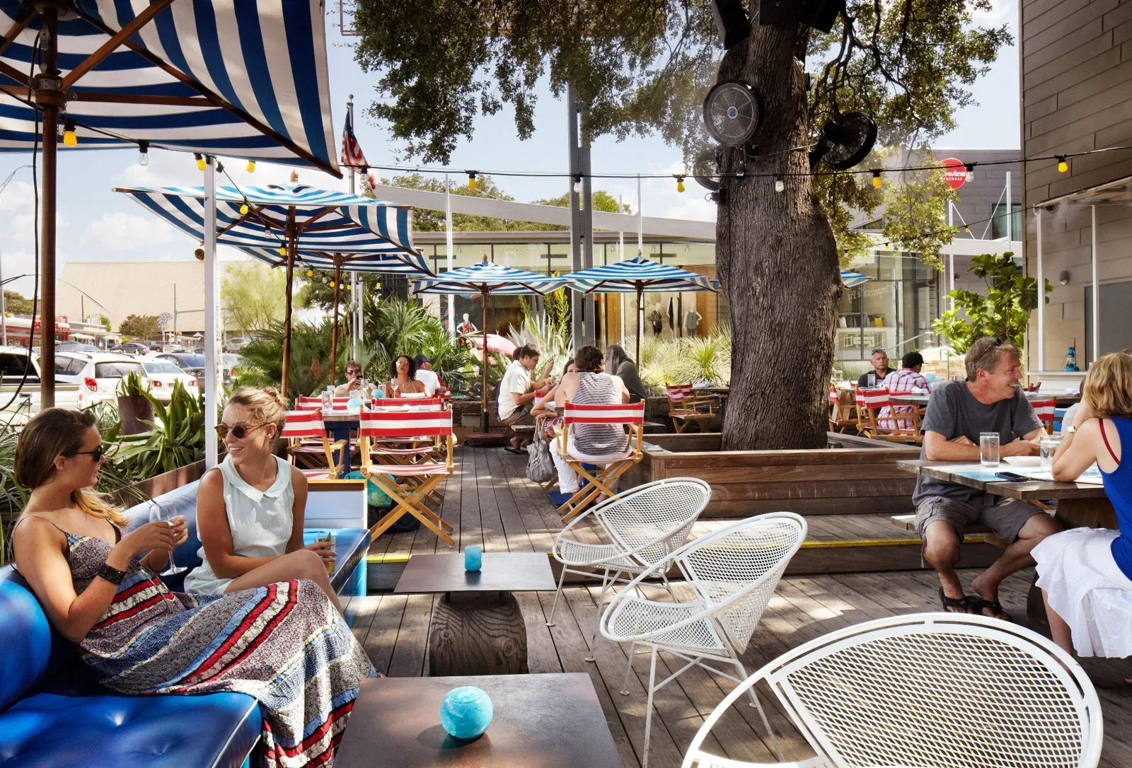 People relaxing on a shaded outdoor restaurant patio with striped umbrellas and string lights in Austin